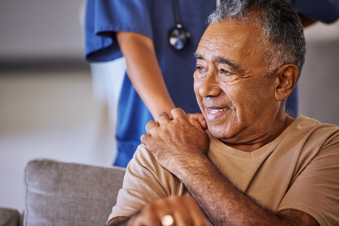 A senior client smiling with his uniformed caregiver close by