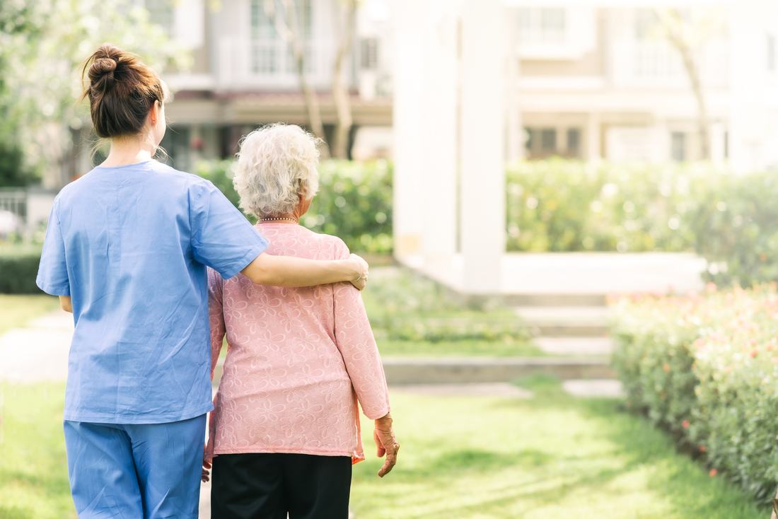 A uniformed caregiver walking outdoors with a senior client