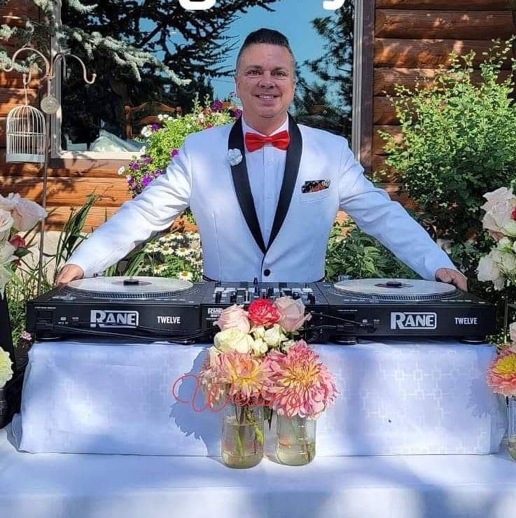 DJ Sugar in a white tuxedo with red bow tie at a garden wedding