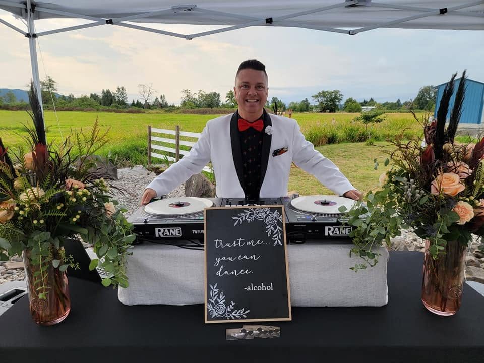 DJ Sugar in a white tuxedo at an outdoor tented wedding